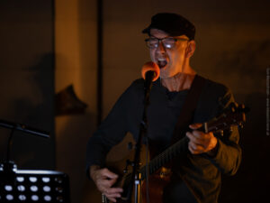 Der Sänger und Gitarrist Roland Kovacs von der Band Rolandrea im Garten von Eva Jansenberger bei der Vernissage zur Ausstellung Möbiusflächen in Trieben 2023, (c) Tom Monochrom